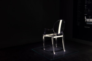A photo of a transparent acrylic chair in a dark exhibition gallery.