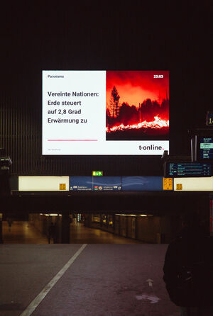 A digital billboard at the Hamburg train station with a news item saying 'earth on track for 2.8°C of warming'