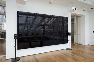 A picture of a large screen on a wall. The screen is black with a white text in the center that reads: You are looking at the sky above this building